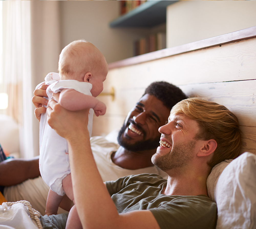 Couple in bed with one partner holding up a new baby